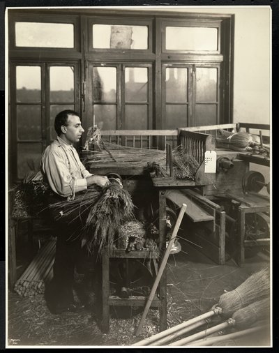 Blind man fastening straw on broom handles at the Bourne Memorial Building, New York, 1921 by Byron Company